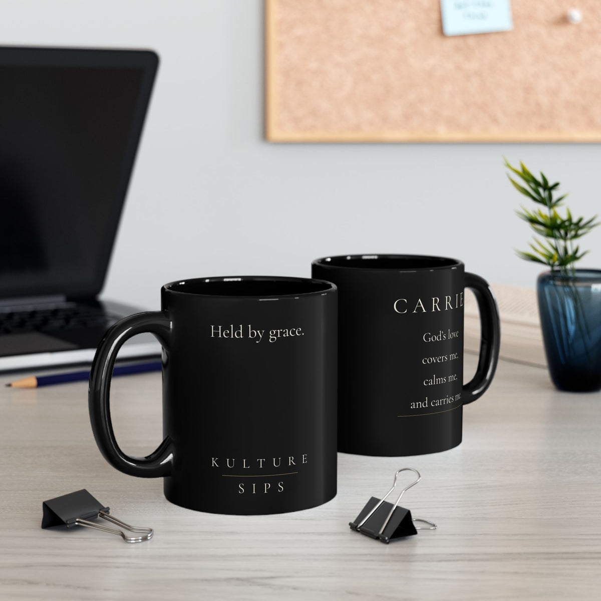 Carried Grace Collection black mugs displayed on office desk, showing front and reverse designs